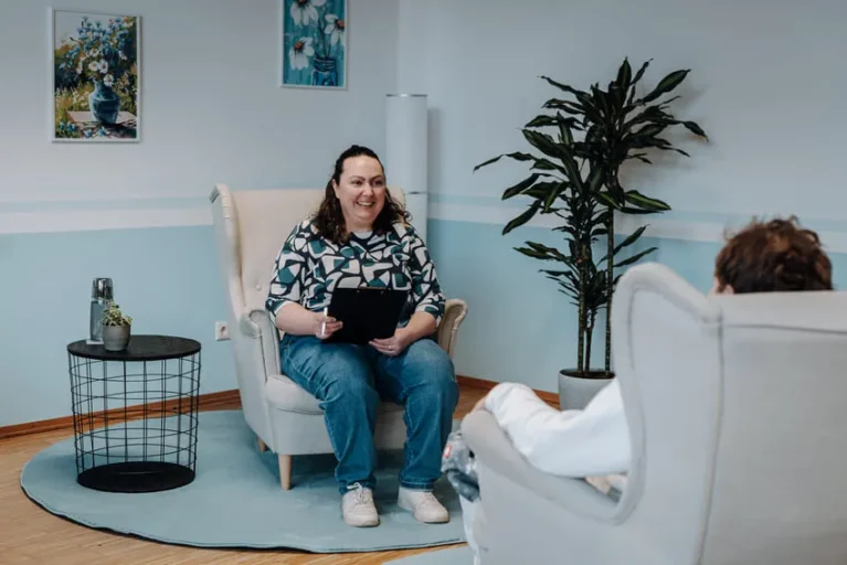 Heilpraktikerin im Gespräch mit einem Patienten, in einem hellen, gemütlichen Raum mit Pflanzen und Kunstwerken.